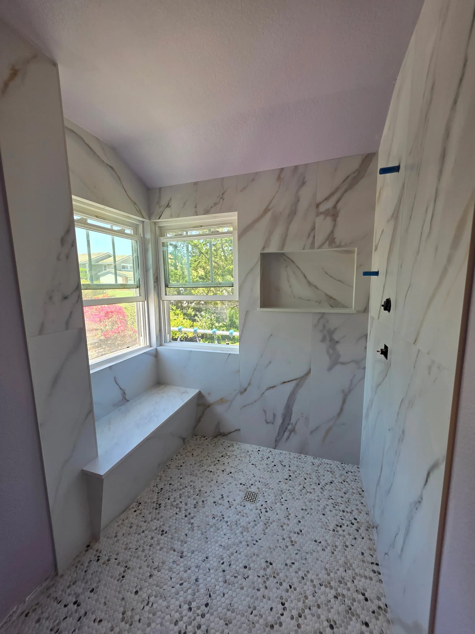 Marble-look tile shower with a built-in bench, recessed niche, and pebble floor